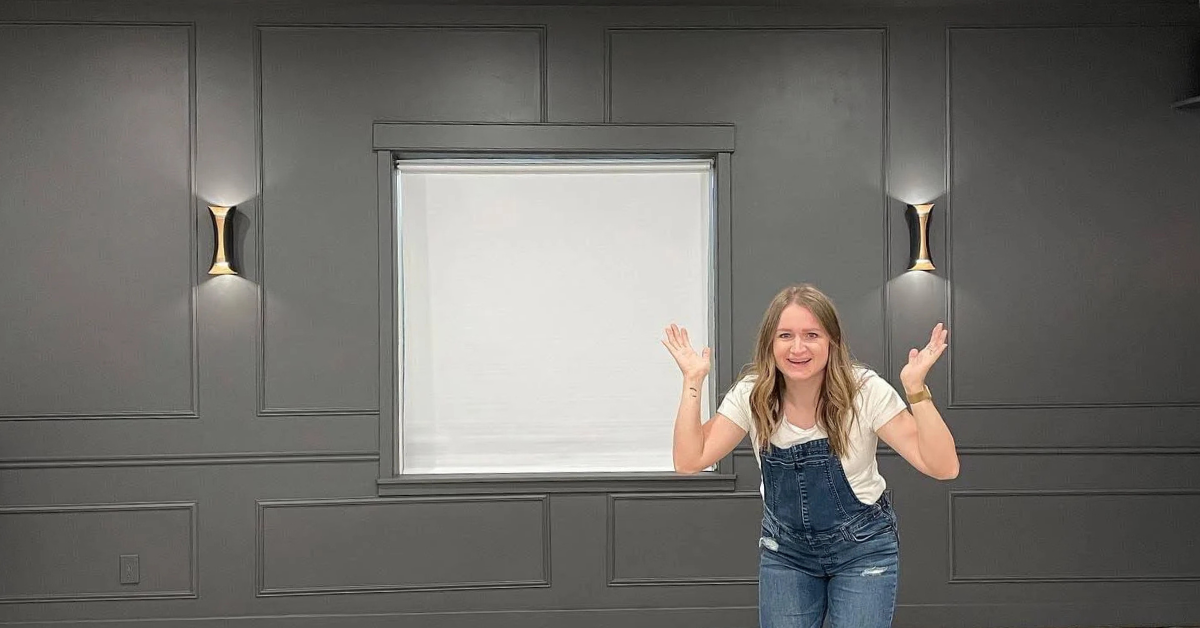 Woman standing in a basement home theater with dark walls, sconces, and a shade over the window