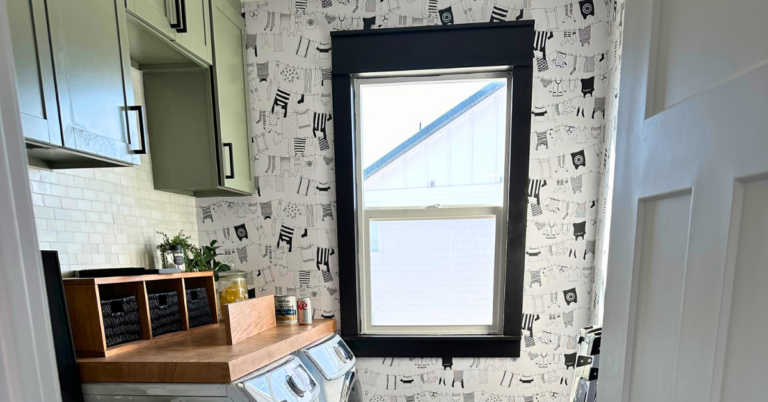 DIY Window Trim in a laundry room with clothesline wallpaper, sage green cabinets, and a wooden laundry shelf over side-by-side washer and dryer
