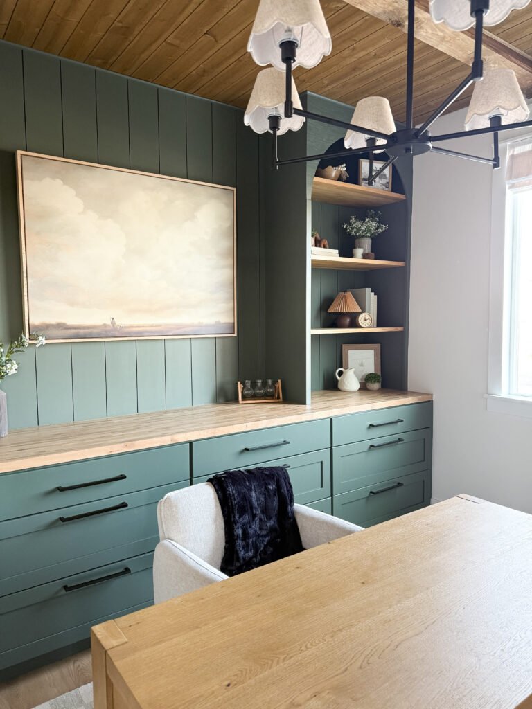 Dark green built-in cabinets and drawers with a light wood desk