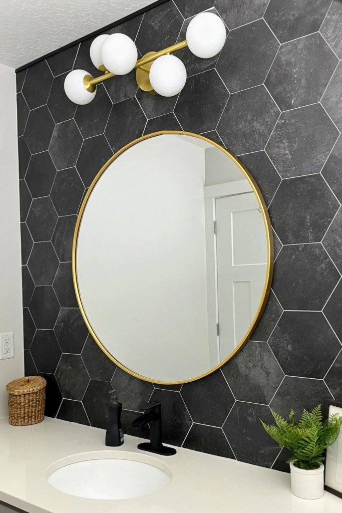 Weekend DIY home projects idea: Update bathroom mirror and light fixture. This photo features black hexagonal tile, a gold circular mirror, and gold mid-century modern light fixture