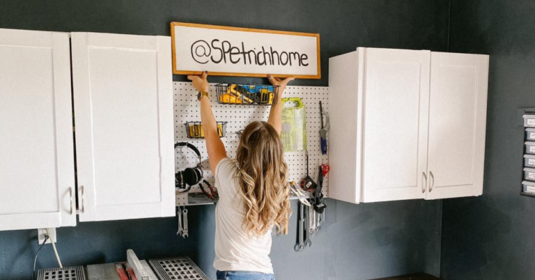 Woman in a workshop lifting a sign that says @SPetrichhome