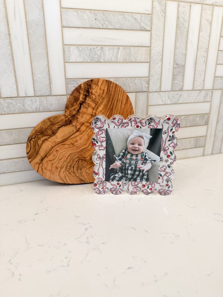 Decoupage picture frame with scalloped edges and cherry/bow print, placed on the kitchen counter in front of a heart-shaped cutting board