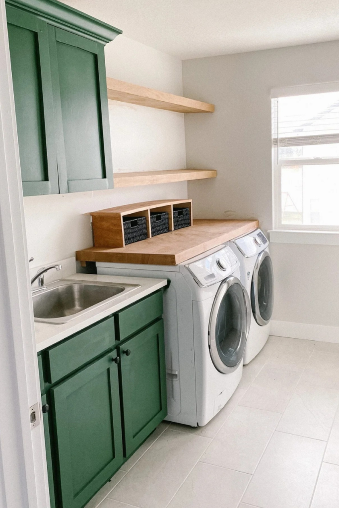 Laundry room with green cabinets and a light wood shelf over side-by-side washer and dryer. Floating shelves above it. 