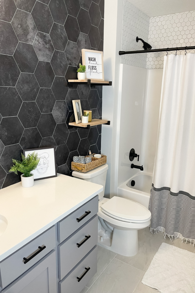 Kids bathroom with black hexagonal tile backsplash, floating shelves, and gray cabinets