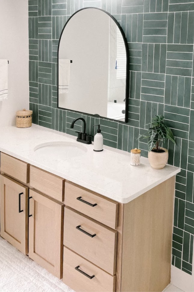 How to choose cabinet hardware example with dark green wall tile, an arched black mirror, white countertops, and light oak cabinets with modern black handles