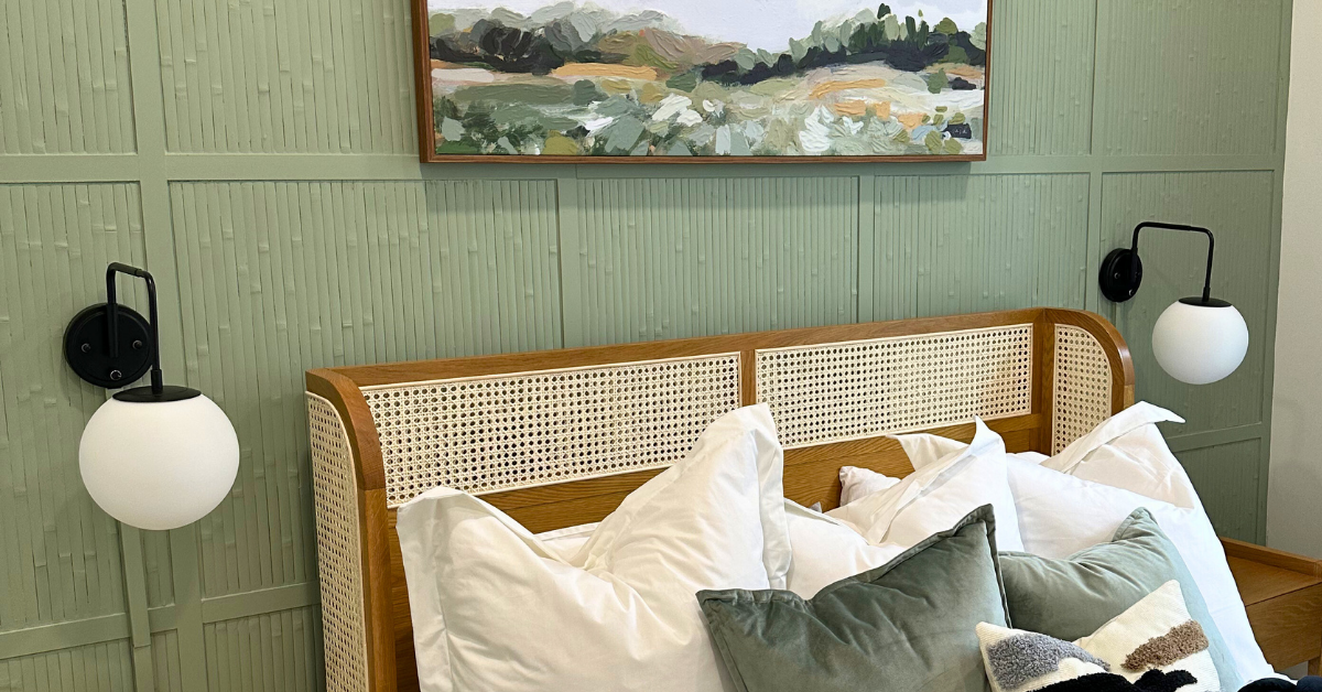 Sage green bamboo accent wall with light wood bed frame, throw pillows, and light fixtures. Light fixtures are hidden by using tips on how to hide cords from wall lights