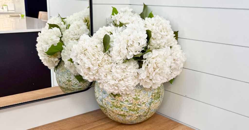 Decoupage vase with white hydrangeas sitting on a light wood entryway table