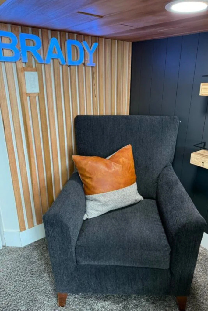 Black armchair with leather and gray pillow, wood slat accent wall in the background