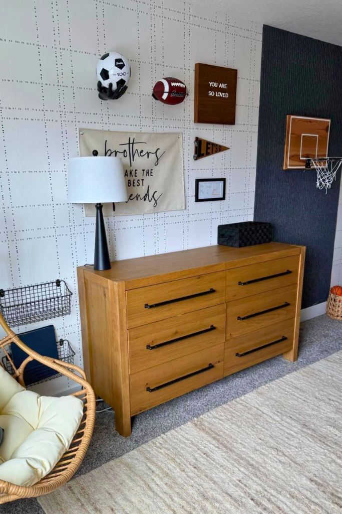 Gallery wall with sports memorabilia and a canvas sign that says "brothers make the best of friends"; light wood dresser against the wall