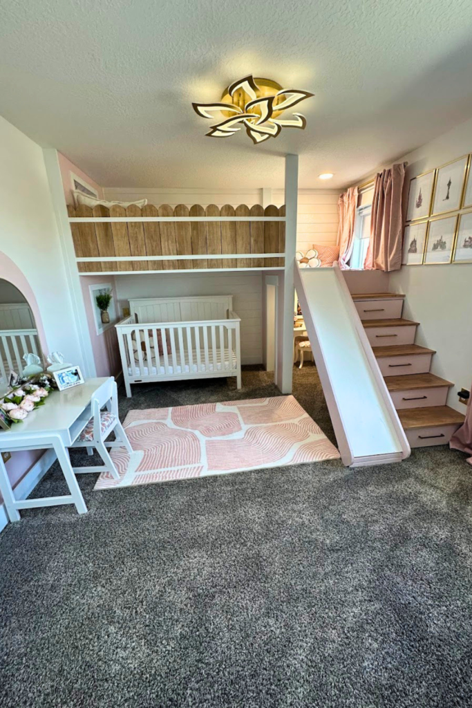 Girls room with loft bed, slide, and stairs; white crib underneath; pink and white rug; white desk