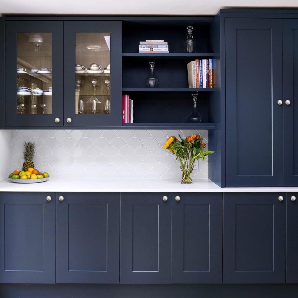 Navy kitchen cabinets with brushed nickel knobs. White countertop and some open/glass upper shelving