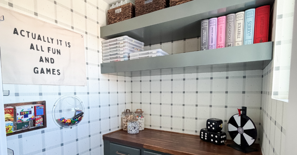 Decor in our game room closet including a sign that says "Actually it is all fun and games"; light gray shelves and cabinets with dark brown butcher block countertop; woven baskets on the shelves