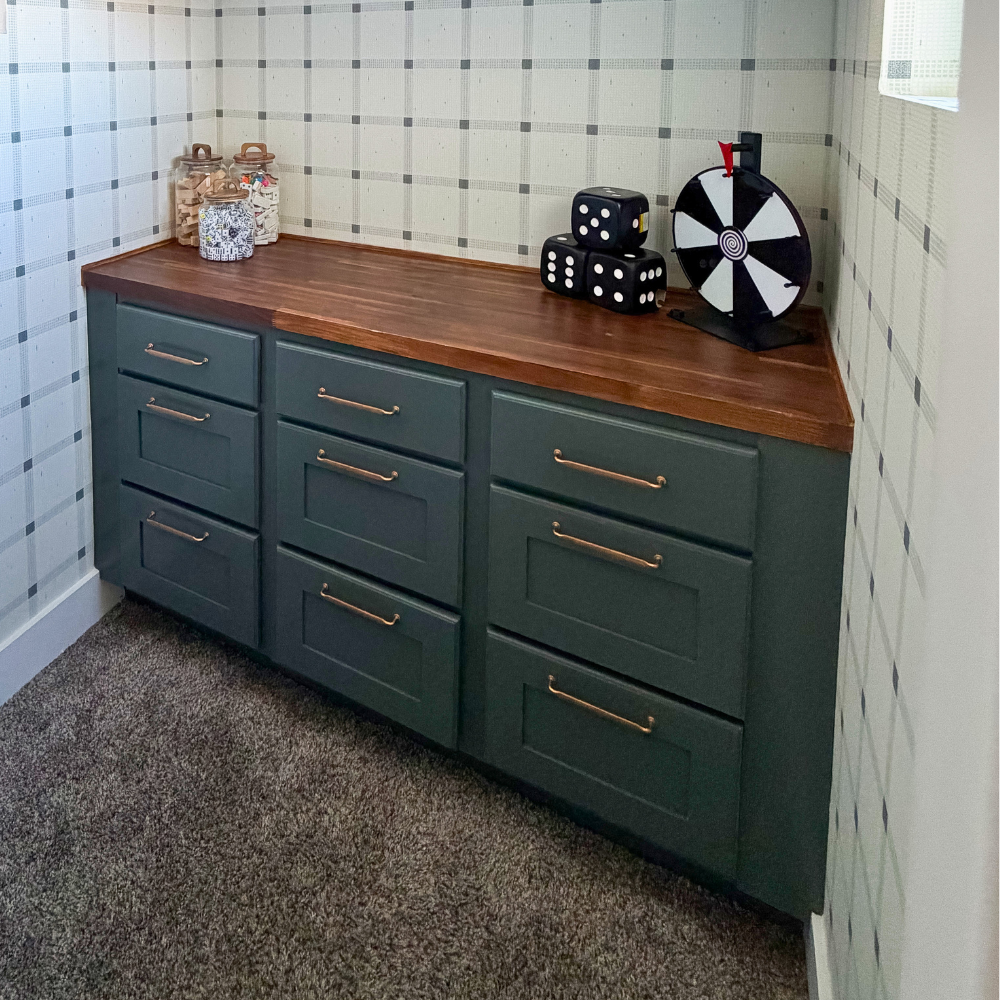 How to Update Cabinets on a Budget: Add brushed gold drawer pulls to dark gray cabinets with a walnut butcher block counter top. Prize wheel toy, oversized dice, and toy containers on top of the counter