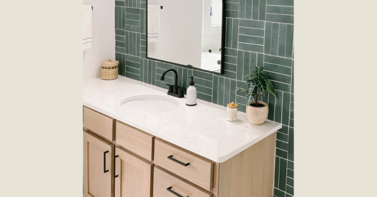 The after of how to replace a bathroom faucet: sleek black hardware on a white counter against a green backsplash