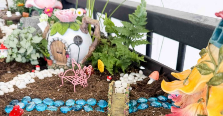 A fairy garden with a turquoise blue stone "river", mini bridge, and mini tea pot fairy house