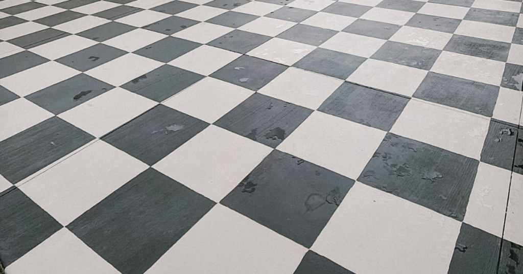 Black and gray checkerboard painted patio with a white vinyl fence