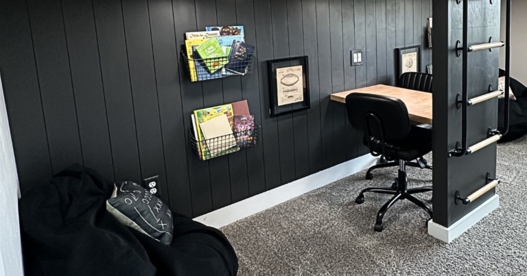 Black shiplap with hanging baskets filled with books, and a desk