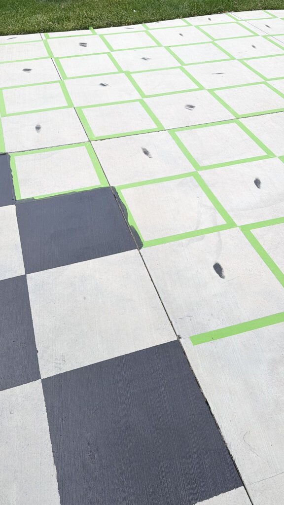 Lime green taped squares on concrete with black paint covering some and black paint marks inside unfinished squares