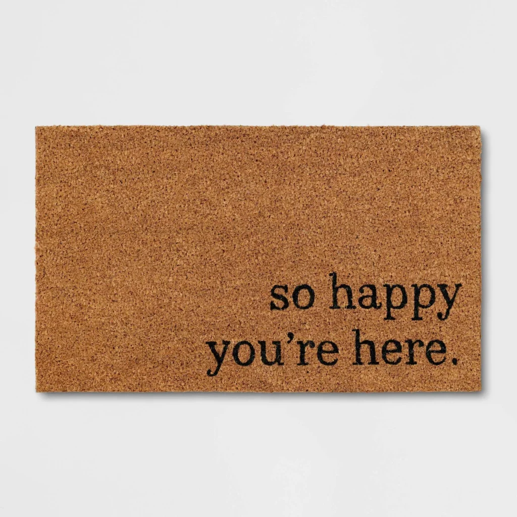 So happy you're here in a lowercase serif font on a doormat
