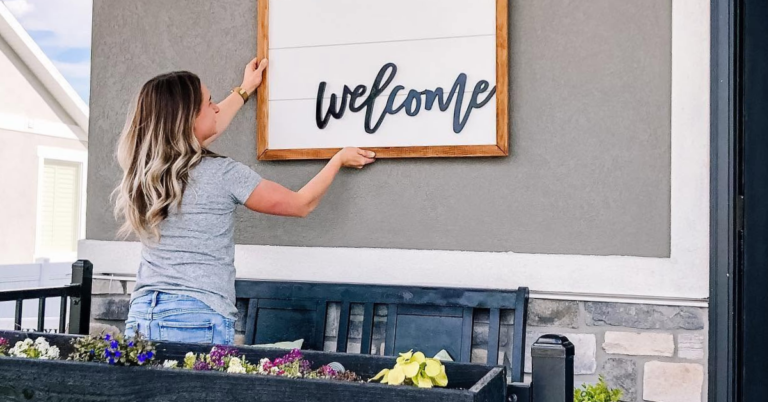 Woman hanging a shiplap sign with welcome written on it as part of a porch makeover