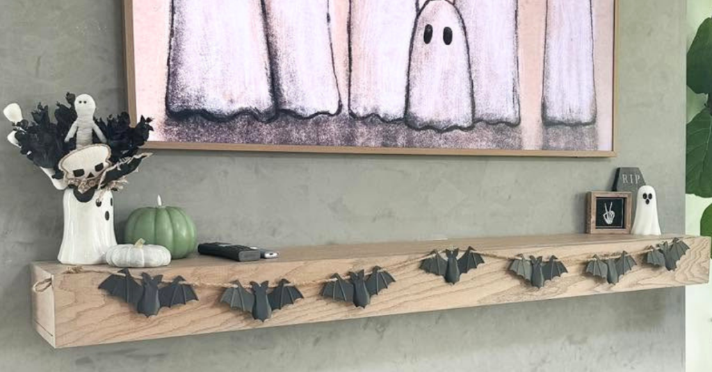 Example of how to style a mantel for every season with a bat garland, ghost art on the tv, and miscellaneous Halloween decorations