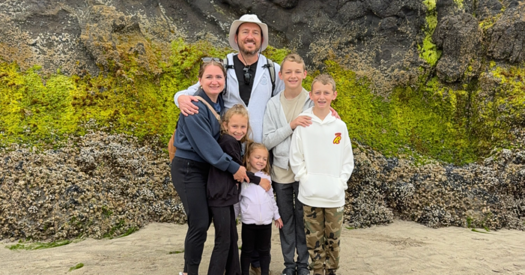 A family visiting the Oregon Coast with kids, standing on the beach in front of mossy rocks