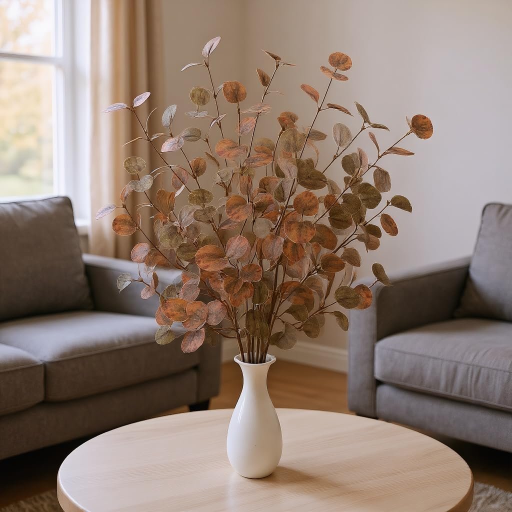 Burnt orange eucalyptus stems ina. small white vase on a table