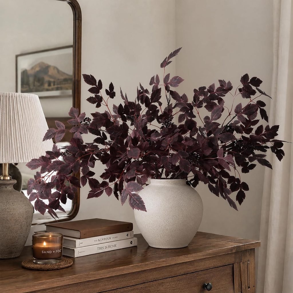 Cimicifuga stems in a cream vase on a wood entry table with books and a lamp on it