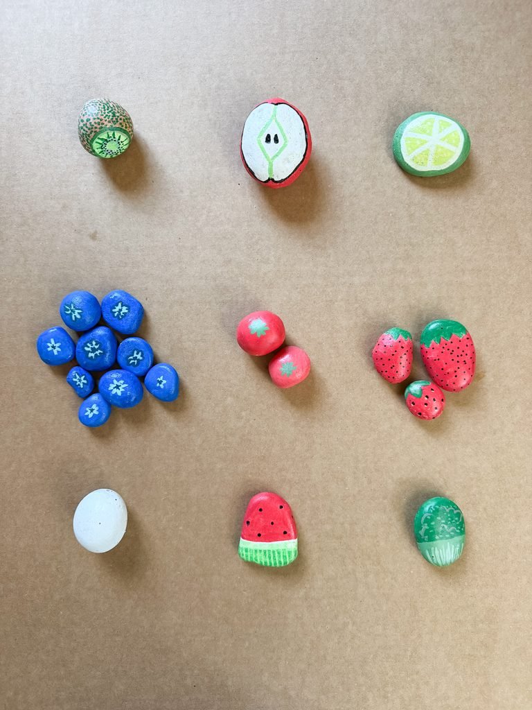 Painted rock food fruit examples including a kiwi, apple, lime, blueberries, and more